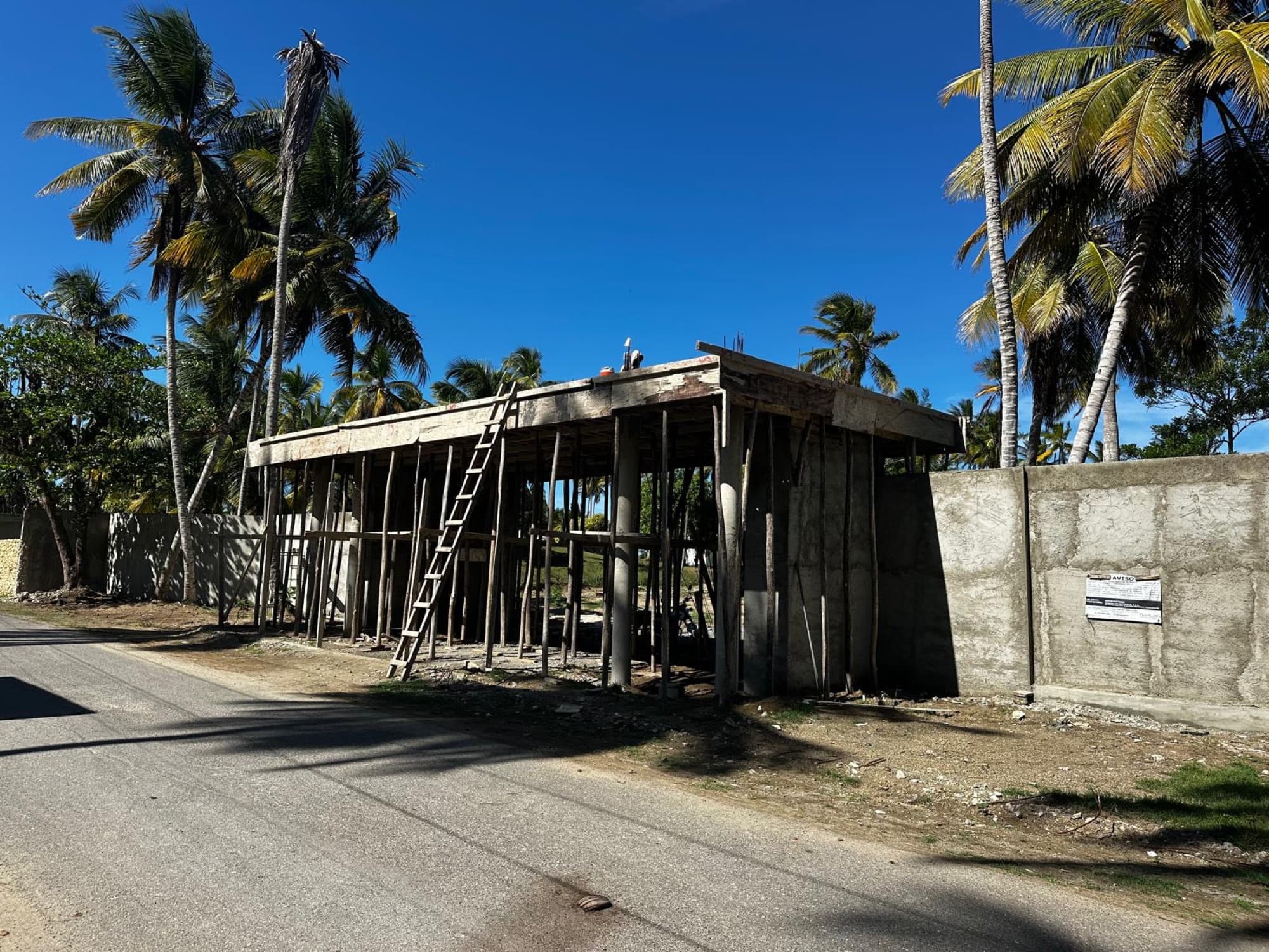 Main entrance: the gate structure with its columns and roof slab in place, the perimeter wall plastered. Finishing work is under way.