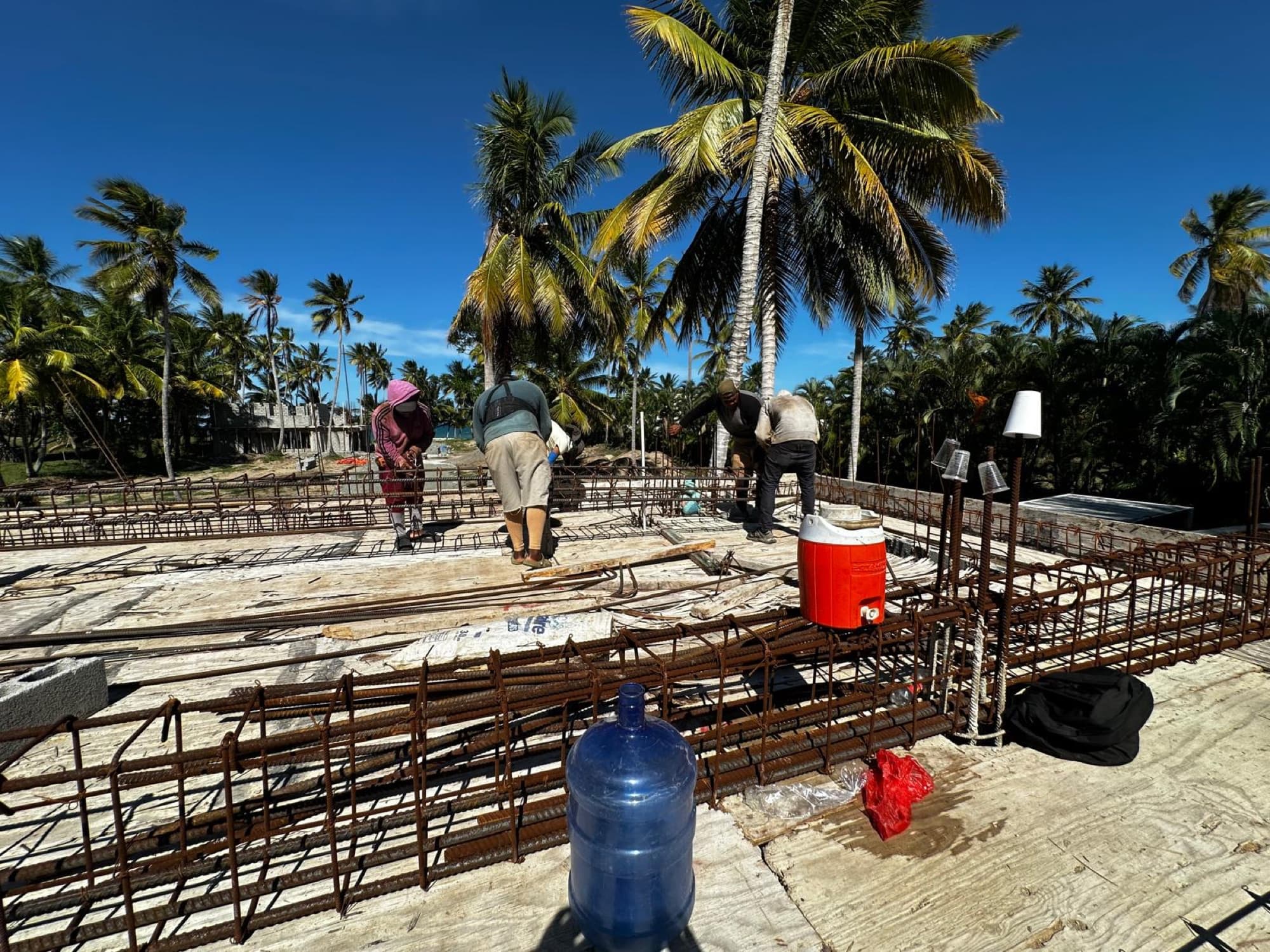 The team tying the steel reinforcement for the ceiling slab, with the beach behind.